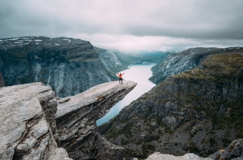 A man enjoying the breathtaking view from the top of Trolltunga, a cliff overlooking a lake.