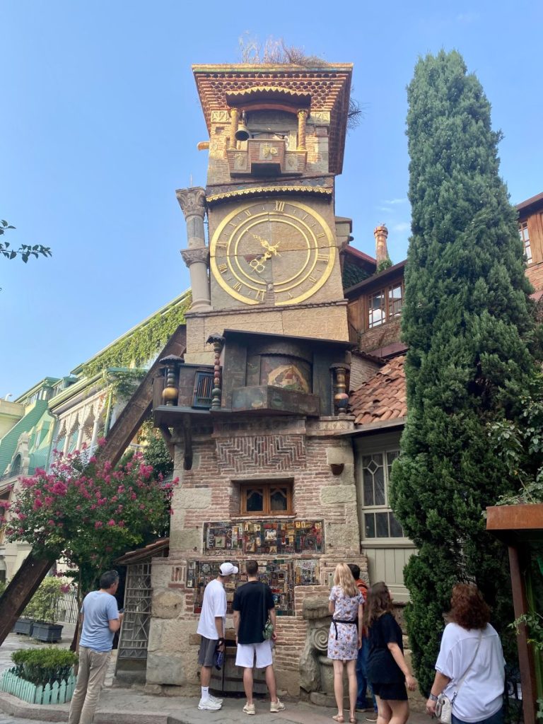 A group of people standing in front of the clock tower in the old town of Tbilisi.