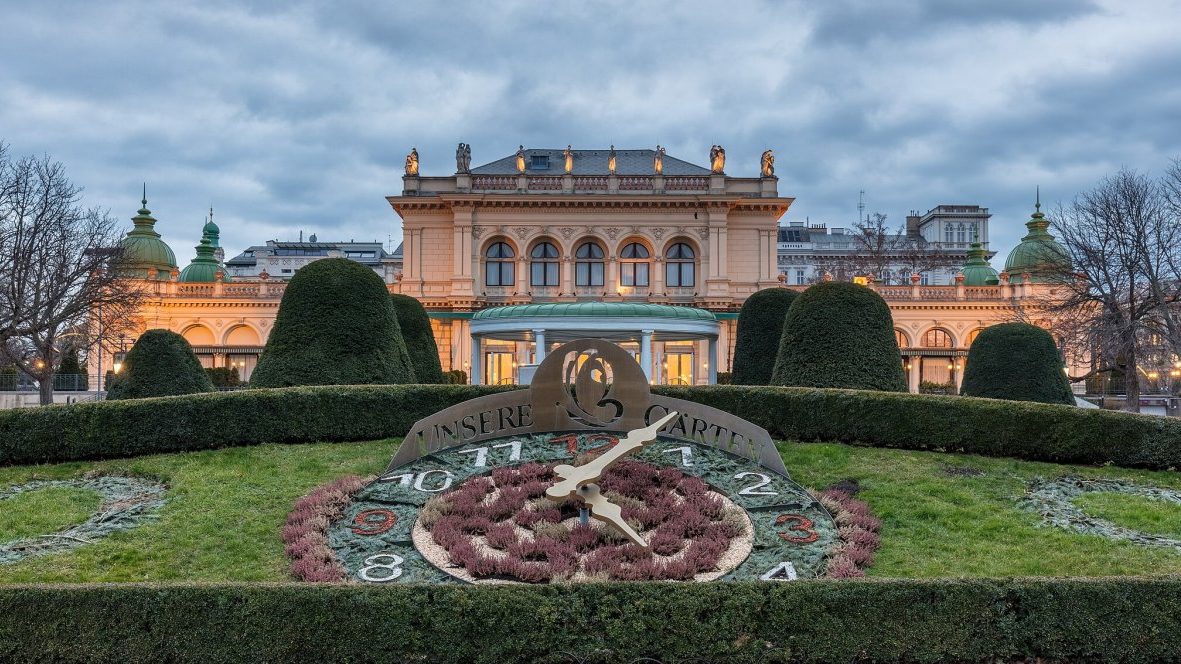 A large clock sits in front of a large building in stadtpark.