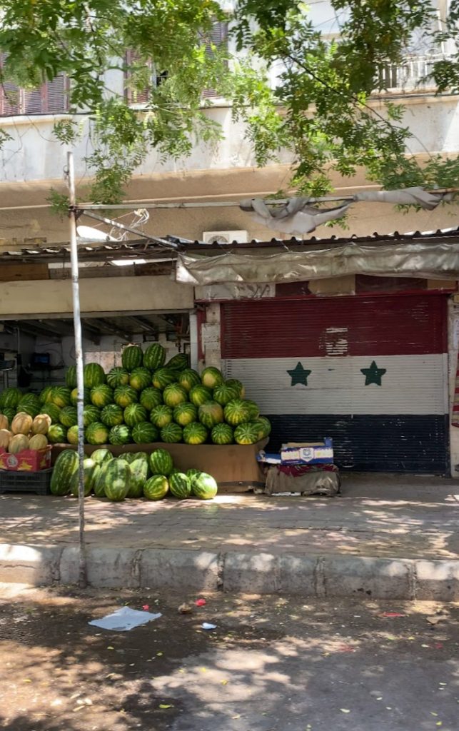 Driving to Damascus, seeing someone selling watermellons next to a syrian flag-drawn garage