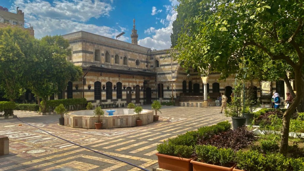  The beautiful courtyard of the Azem Palace. There is a fountain in the middle and many trees and flowers