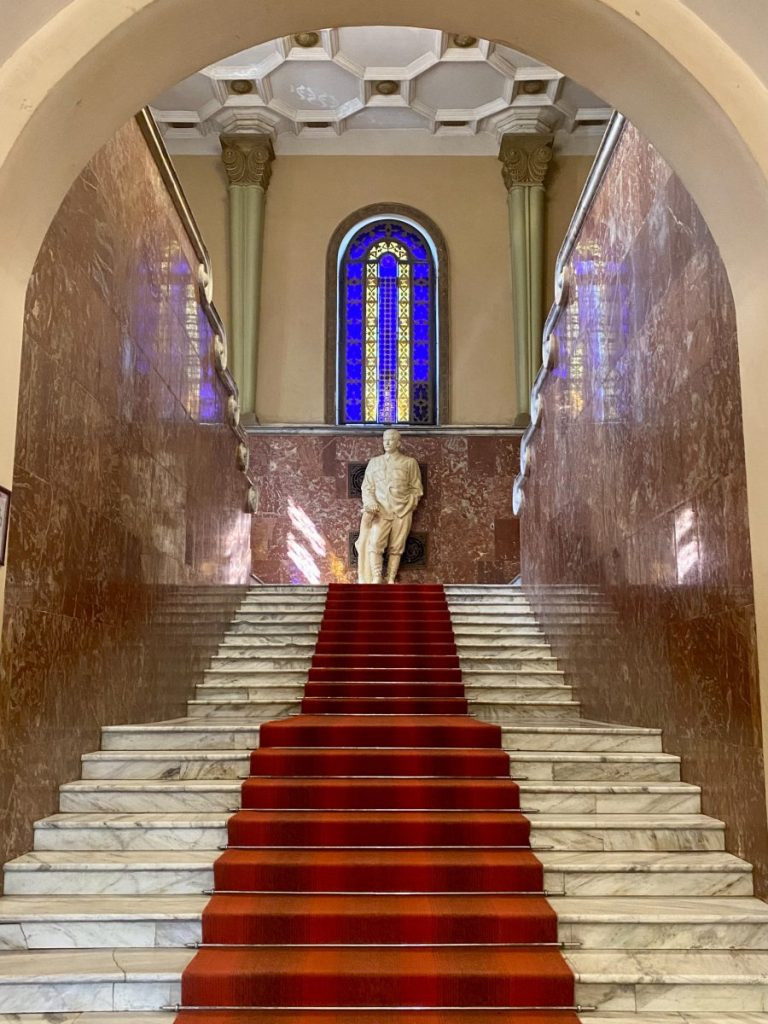 A staircase in the museum building with the statue of Stalin and red carpet.