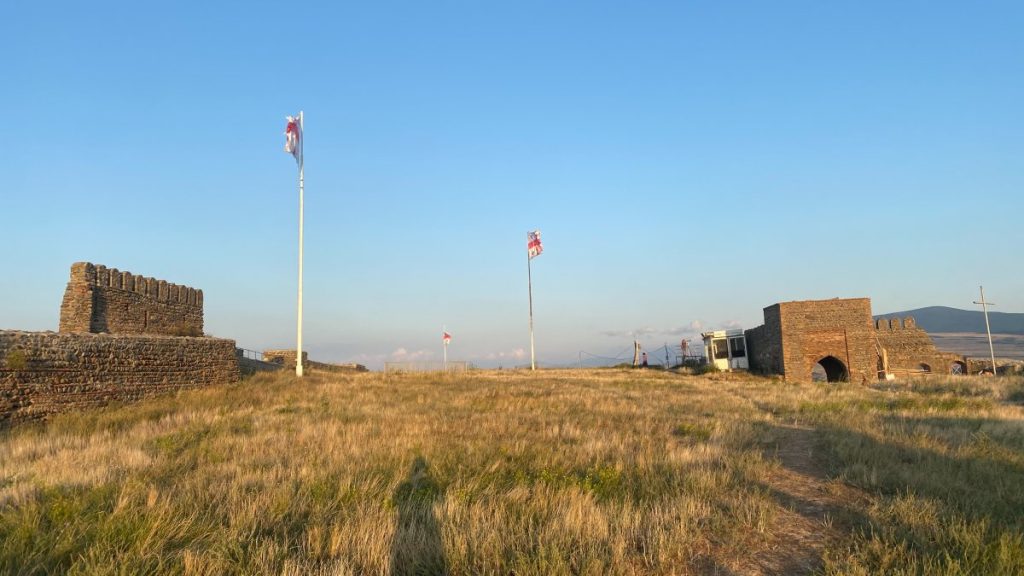 An old fort with flags of Georgia and Gori flying in the grass.