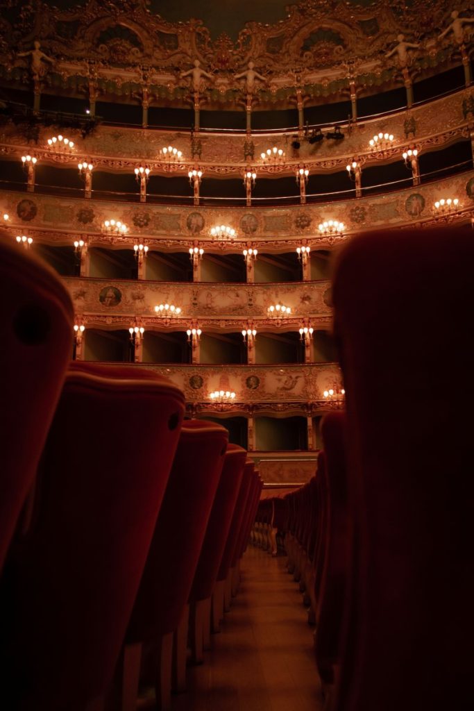 An empty auditorium with red seats and chandeliers, a stunning spot to experience the sensational cultural offerings in Venice.
