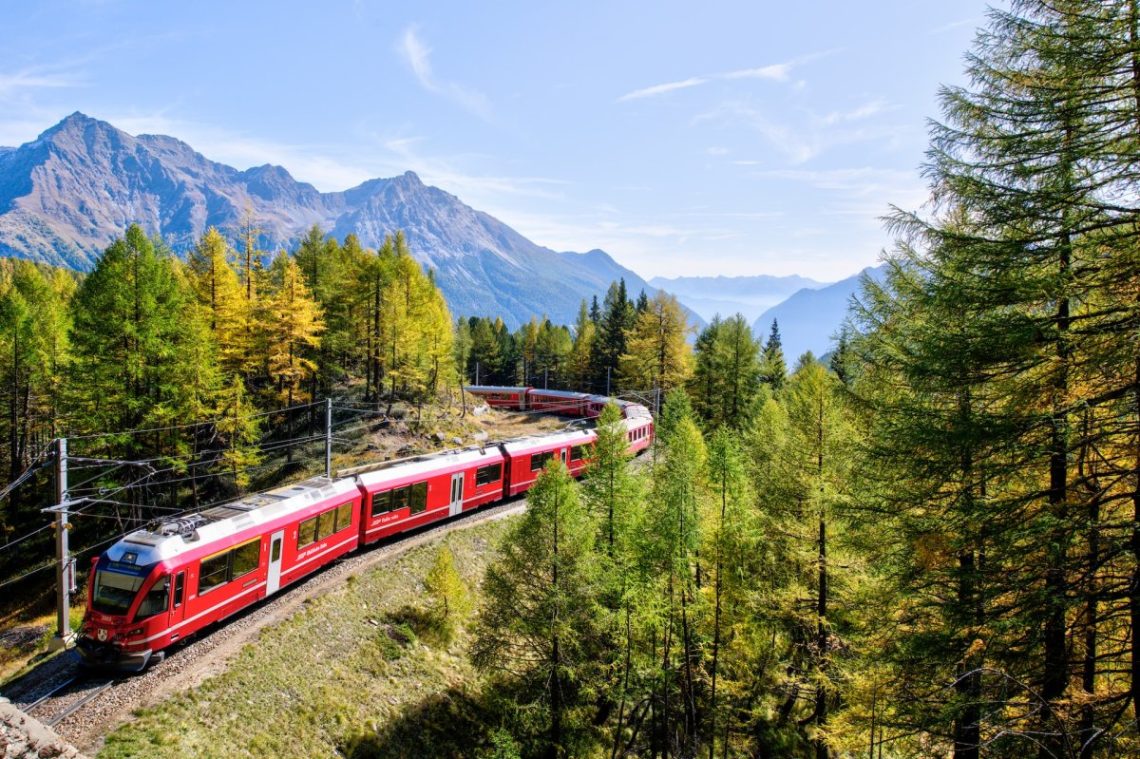 A red train travels through a forest with trees in the background while showcasing what is interrail.