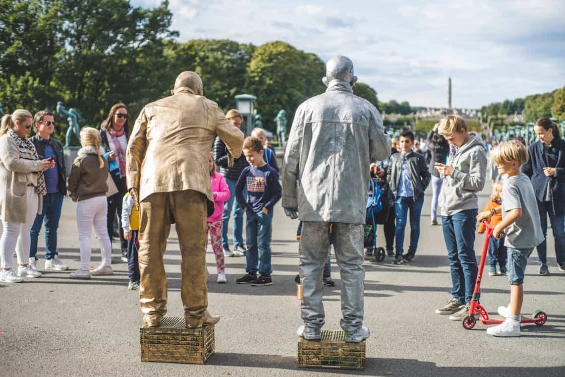 Street performers gather a diverse crowd at Vigeland Park in Oslo for a lively outdoor show.