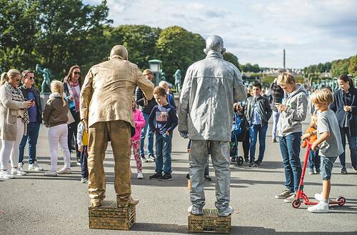 Street performers gather a diverse crowd at Vigeland Park in Oslo for a lively outdoor show.