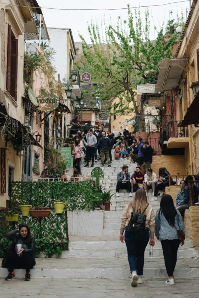 A vibrant street in Plaka filled with people, small shops, and lush trees, capturing the lively atmosphere of a popular outdoor shopping district.