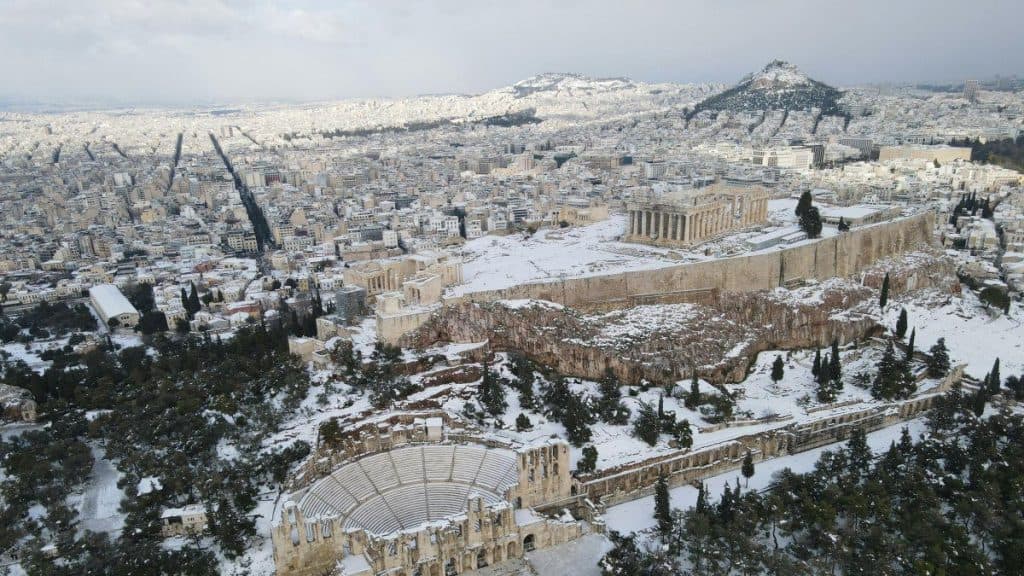 A panoramic view of Athens' Acropolis, including the Parthenon, blanketed in snow, highlighting Greece's rich history and winter landscape.