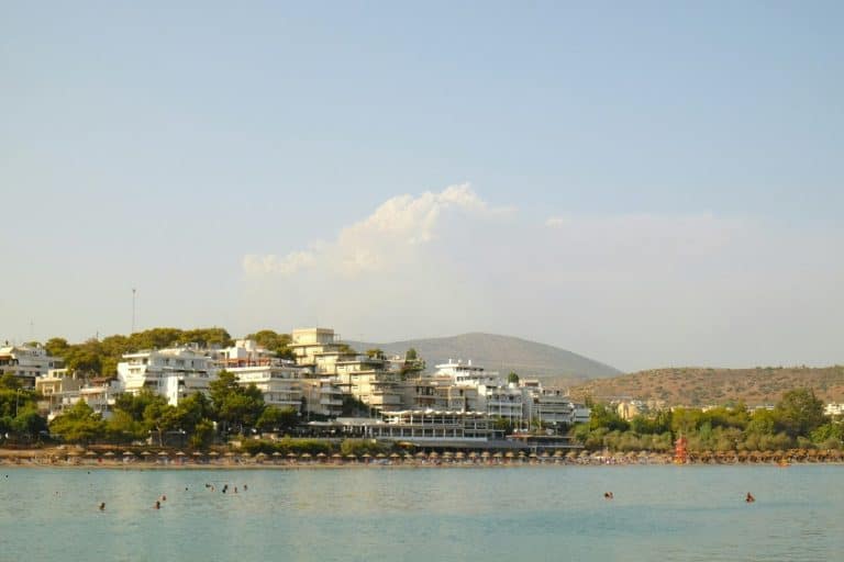 Vouliagmeni in Athens, Greece during a summer afternoon. Four seasons palace is visible from afar, and people are enjoying the soft blue waters.
