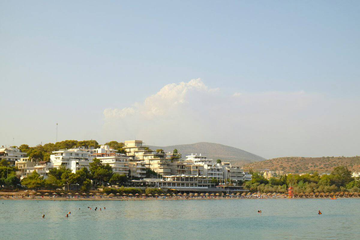 Vouliagmeni in Athens, Greece during a summer afternoon. Four seasons palace is visible from afar, and people are enjoying the soft blue waters.
