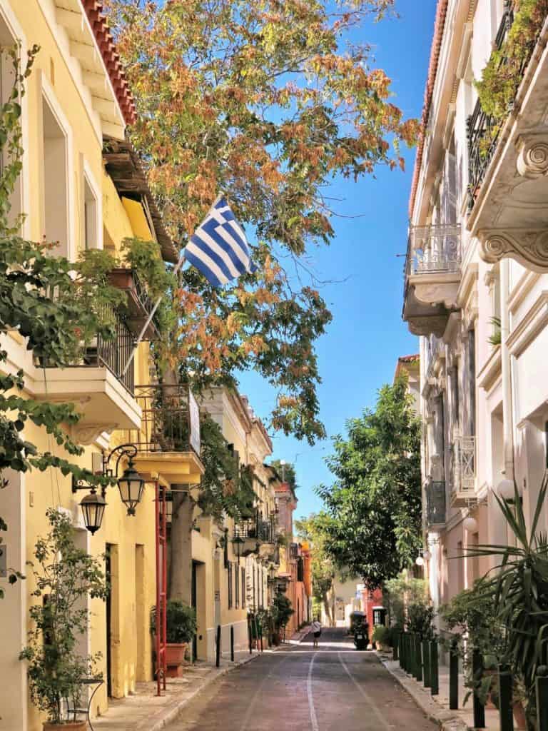 Greek street scene with colorful buildings and a Greek flag under a clear blue sky.