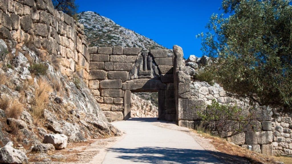The Ancient stone gate in Mycenae surrounded by rocky terrain and greenery under a clear blue sky.