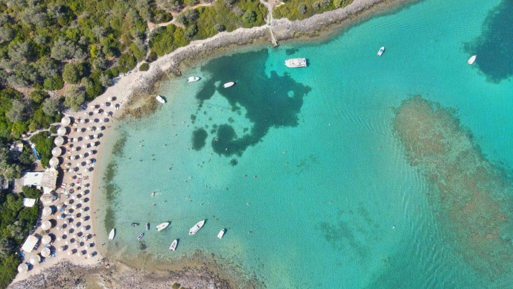 This aerial image captures a peaceful turquoise bay in Lichadonisia with boats anchored near the shore, framed by lush greenery, highlighting a perfect relaxing seaside destination.