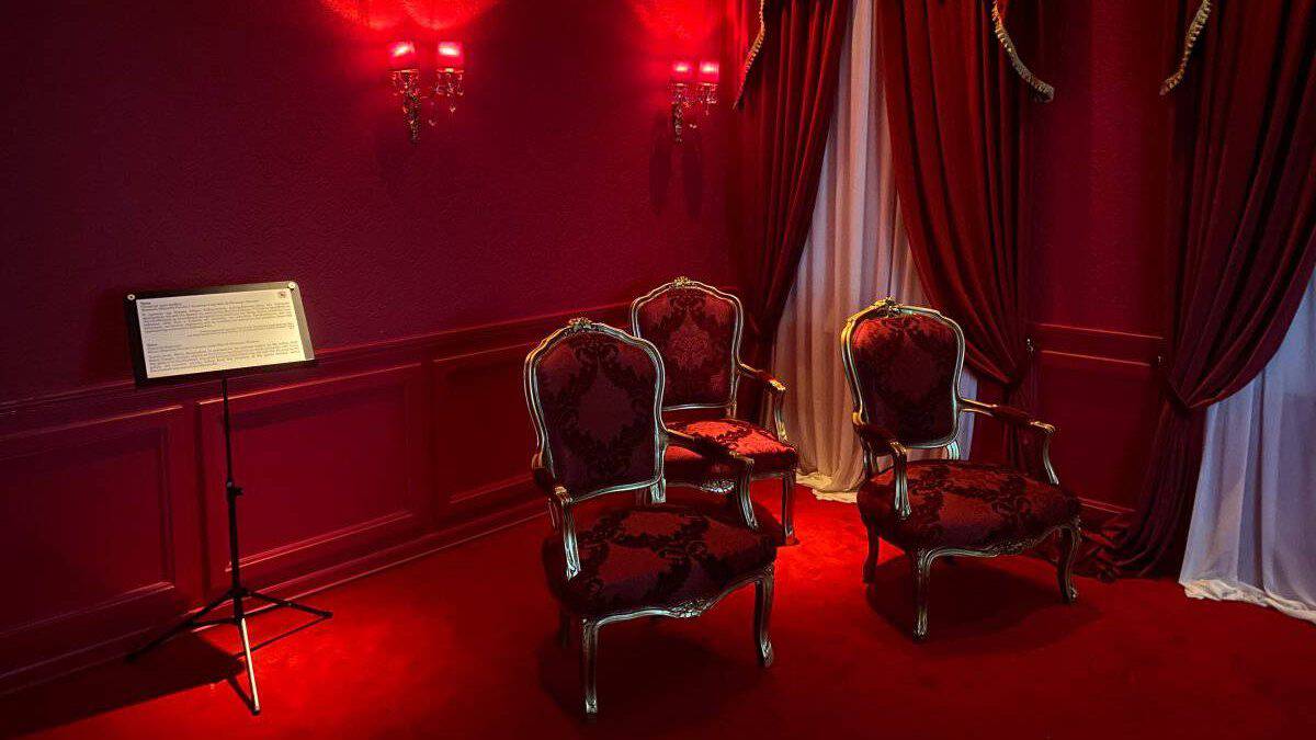 A red room in the Maria callas museum in Athens that is luxuriously decorated. There are red chairs and a black podium.