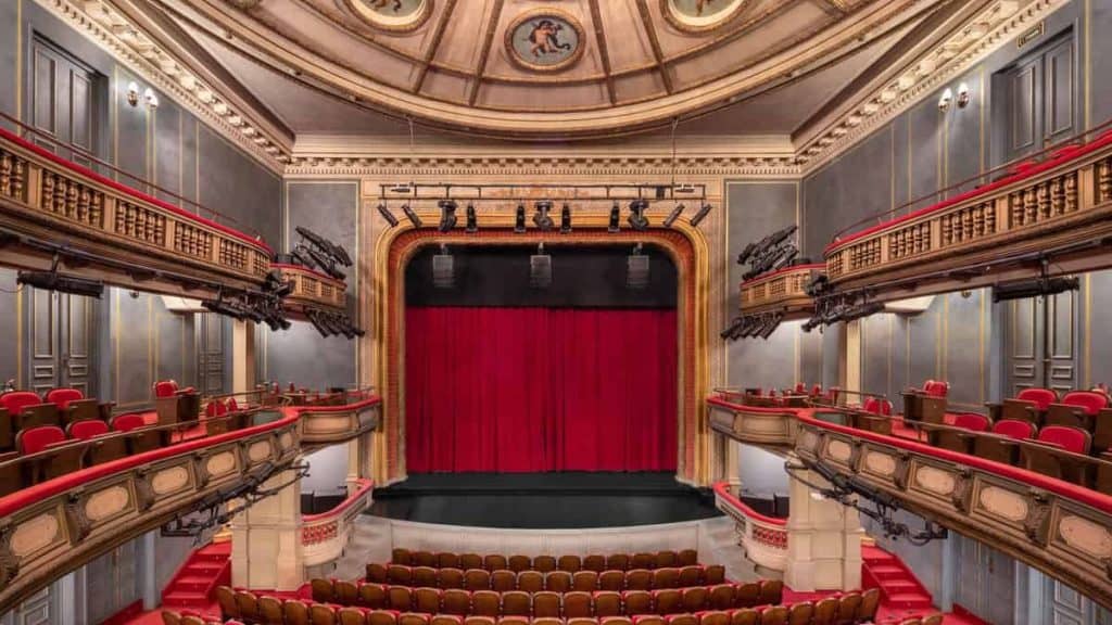 Elegant theatre interior with ornate details and red velvet curtains.