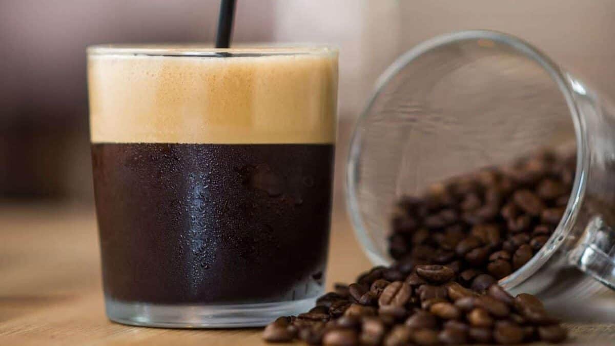 Freshly brewed espresso coffee with crema and coffee beans spilled on the table.